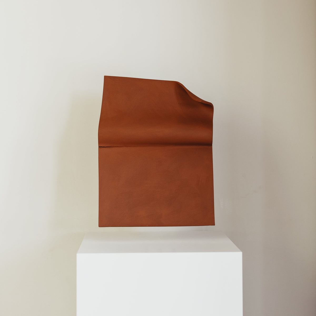 Writings 001 by Studio JOA — Stone Red folded stoneware wall piece displayed on a white pedestal, gallery-style presentation