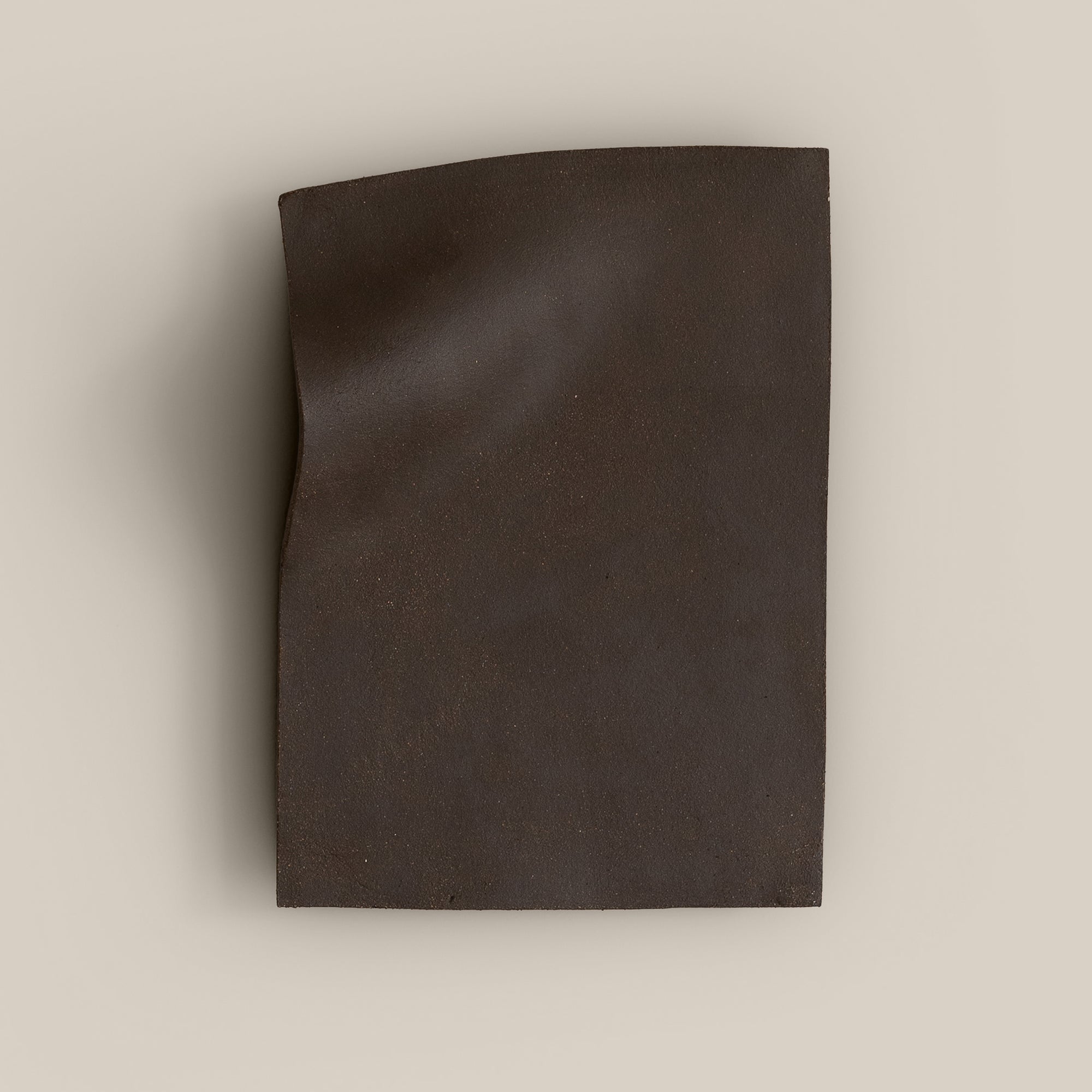 Writings 003 by Studio JOA — Dark Brown stoneware wall piece with a pinched vertical fold along one edge, photographed against a plain wall