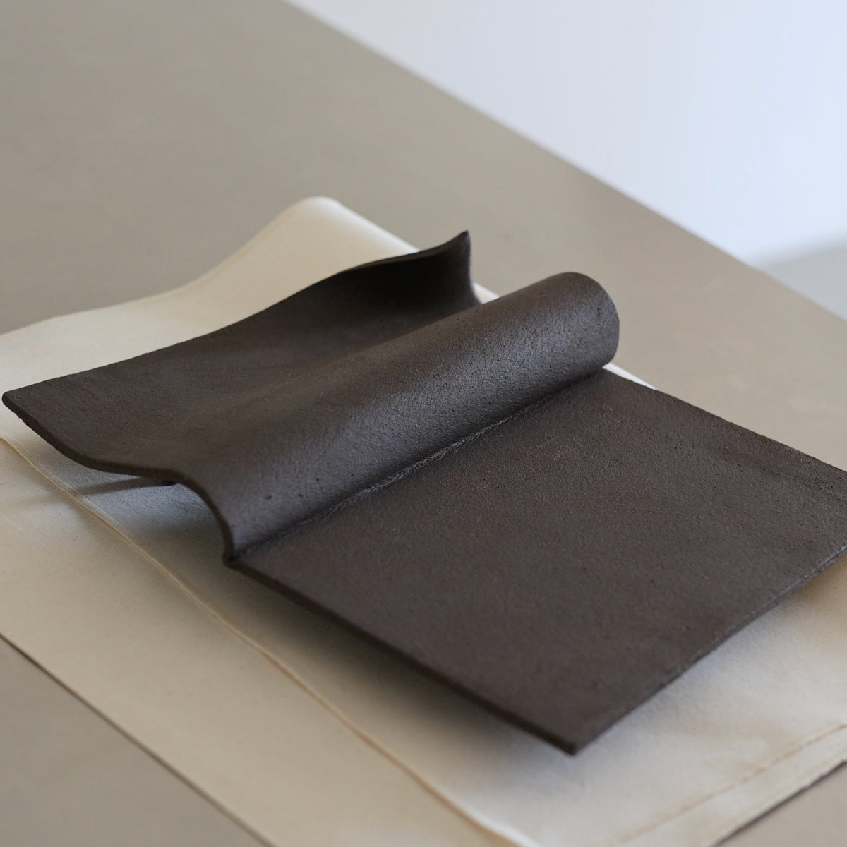 Writings 001 by Studio JOA — Dark Brown folded stoneware wall piece resting on beige fabric on a table