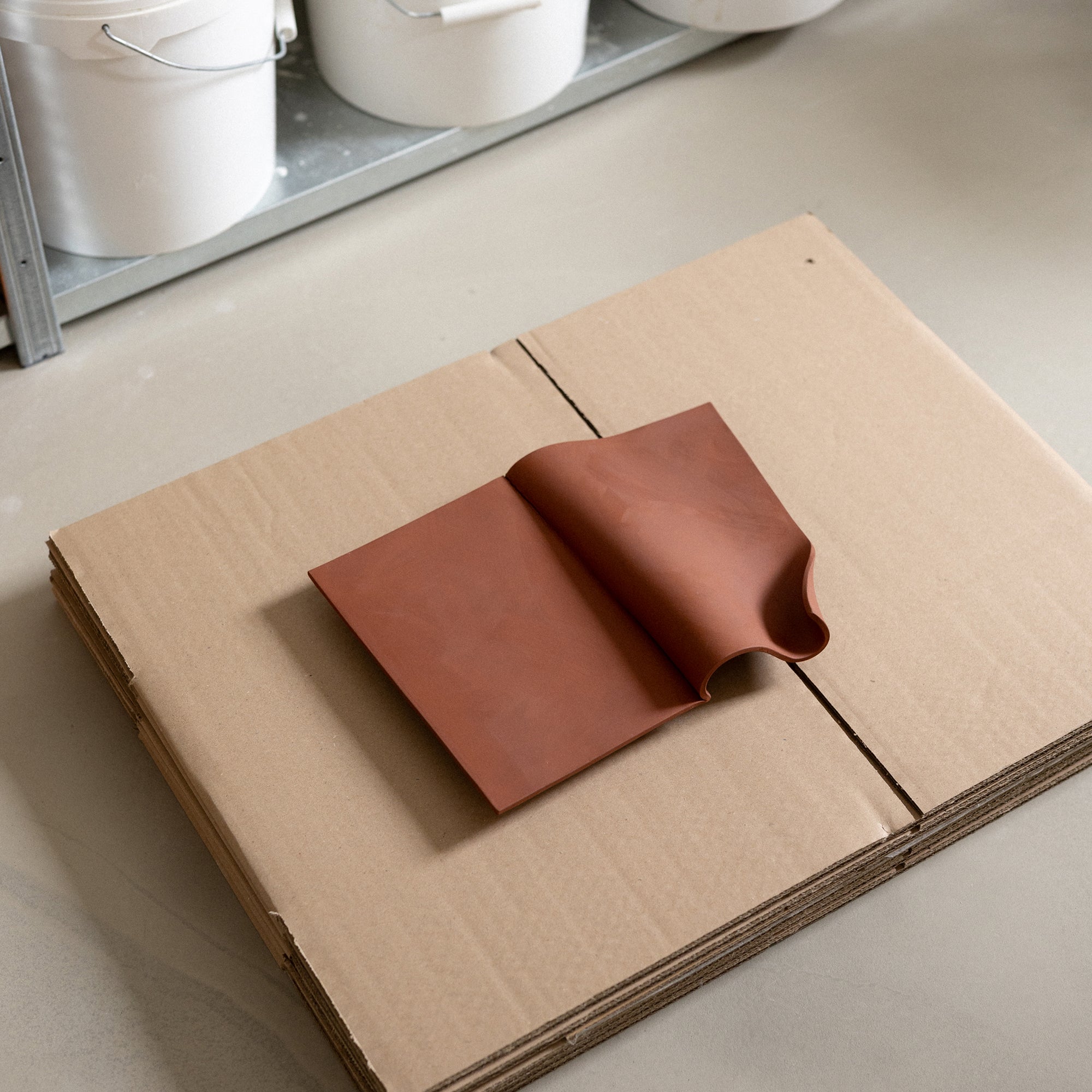 Studio JOA — Stone Red folded stoneware wall piece resting on cardboard in the studio, materials visible in the background
