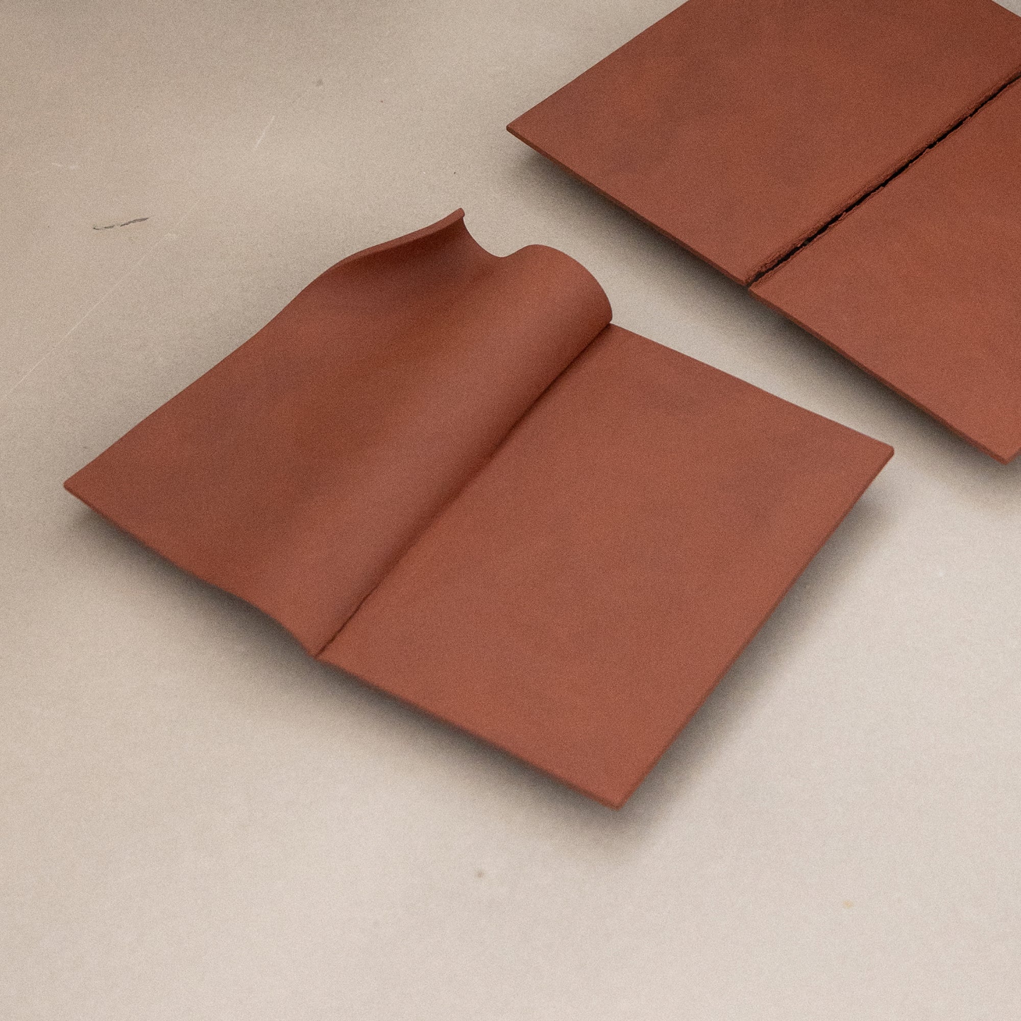Writings 001 by Studio JOA — two Stone Red folded stoneware pieces resting flat on a table