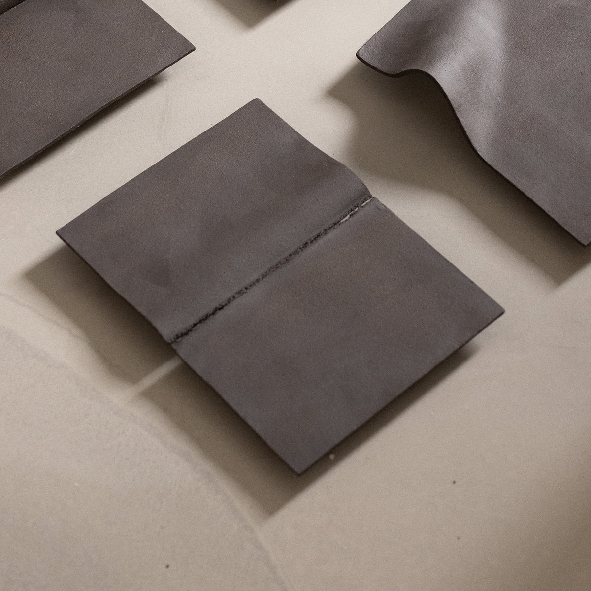 Studio JOA — Dark Brown stoneware wall piece in the studio, resting on a table beside other Writings pieces