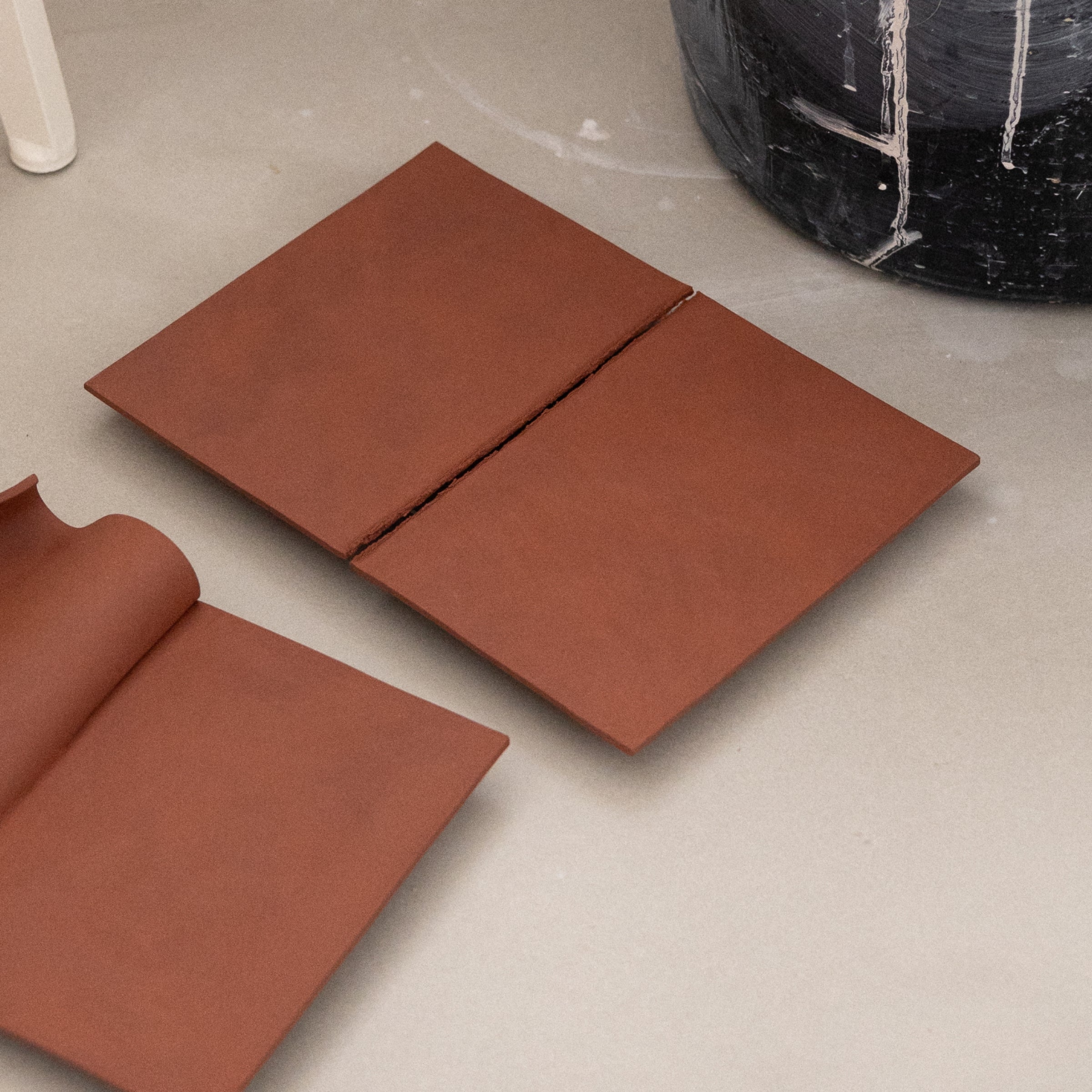 Studio JOA — Stone Red stoneware wall piece in the studio, resting on a counter beside a curled Writings piece and studio materials