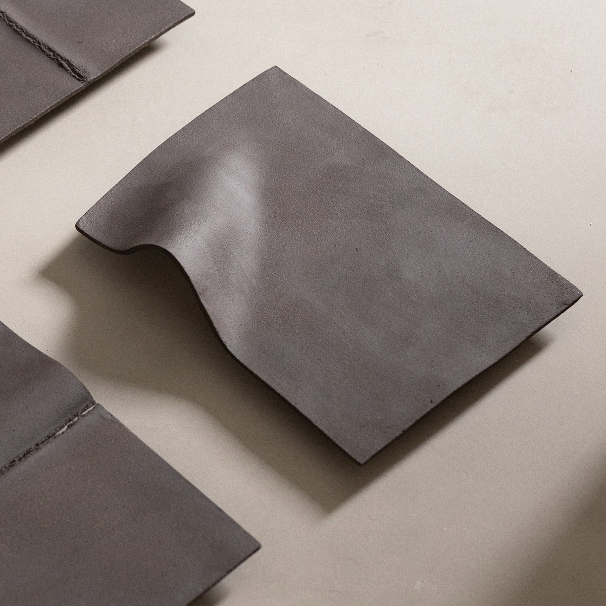 Studio JOA — Dark Brown stoneware wall piece in the studio, resting on a table beside other Writings pieces