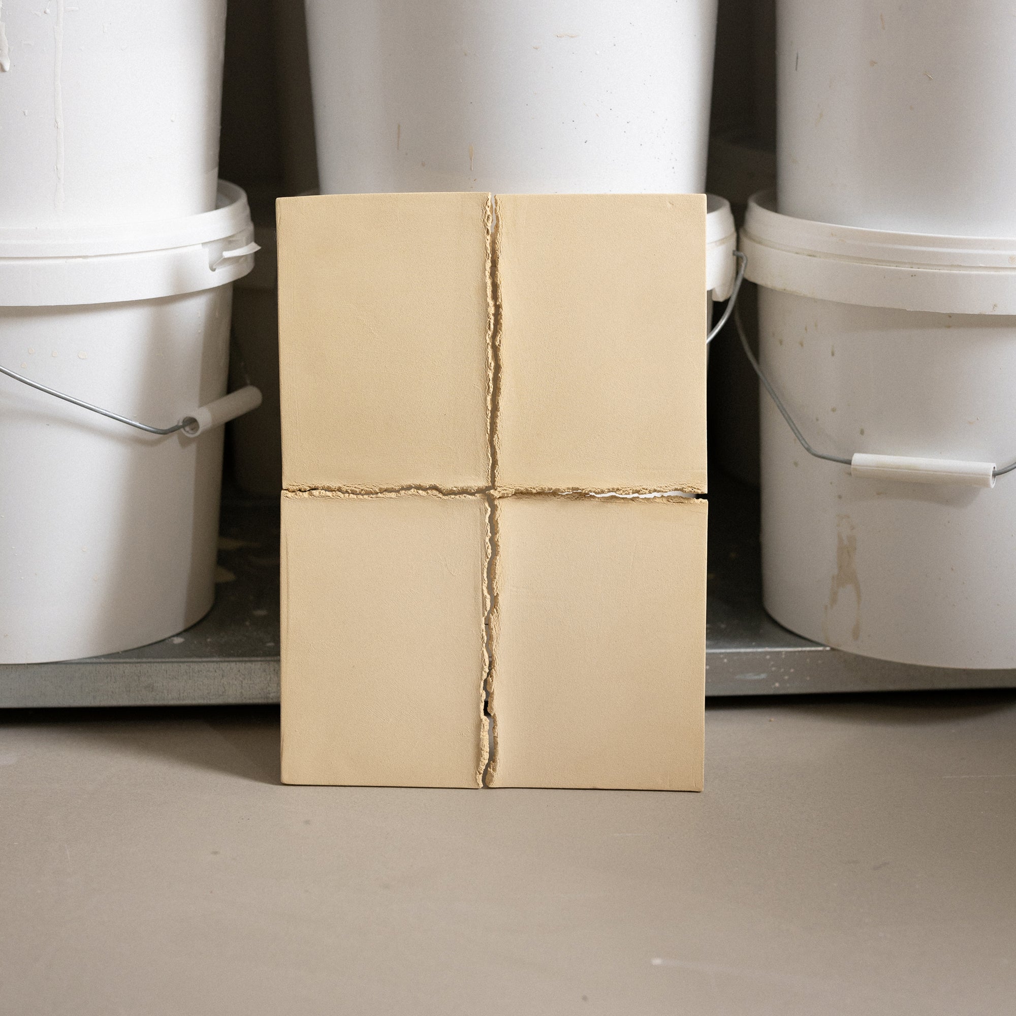 Studio JOA — Butter Yellow stoneware wall piece standing upright in the studio, leaning against storage buckets