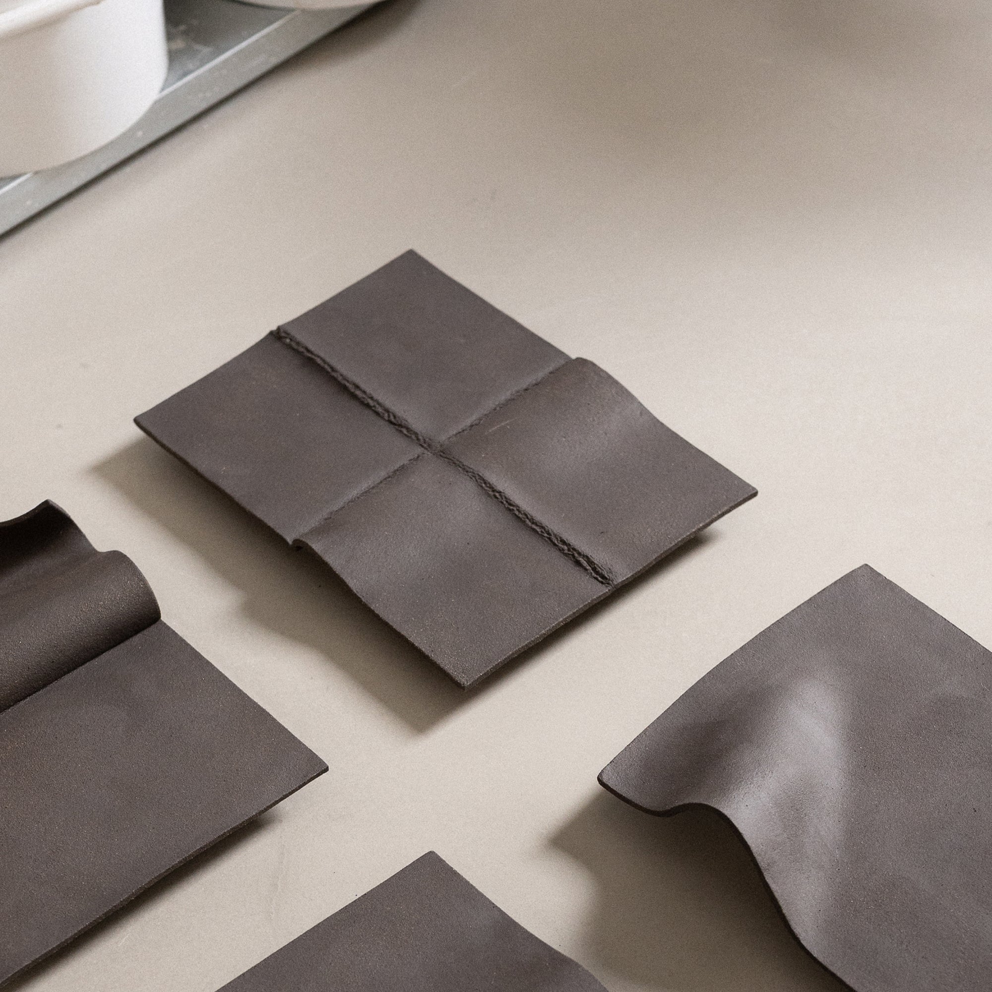 Studio JOA — Dark Brown stoneware wall piece in the studio, resting on a table beside other Writings pieces