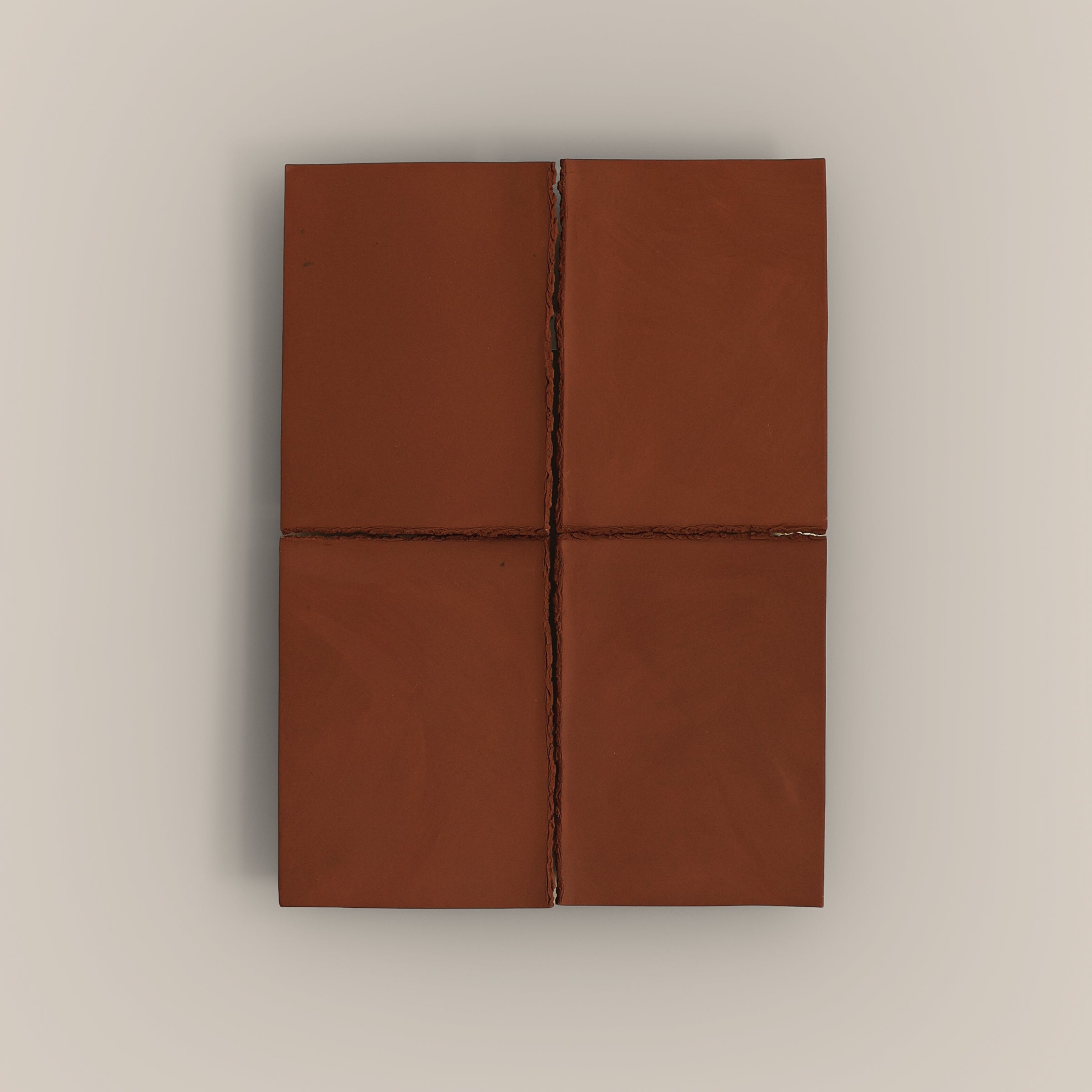 Writings 004 by Studio JOA — Stone Red stoneware wall piece divided into four panels by a cross-shaped seam, photographed against a plain wall